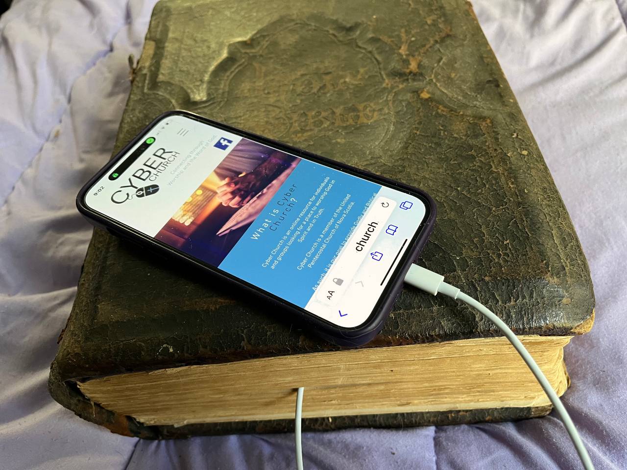 An antique bible has an iPhone plugged in to the pages. 