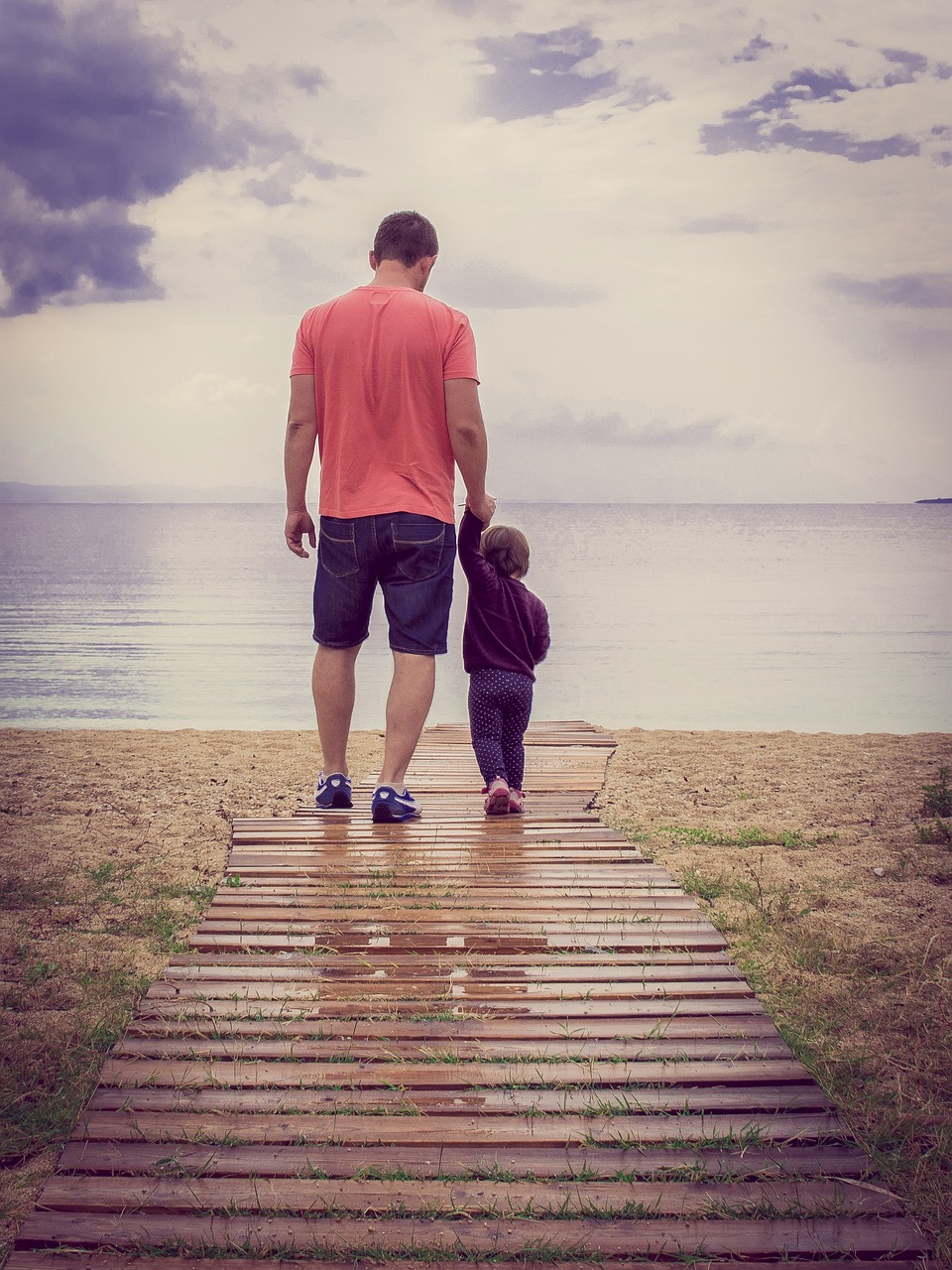 A father and daughter walk towards the water.