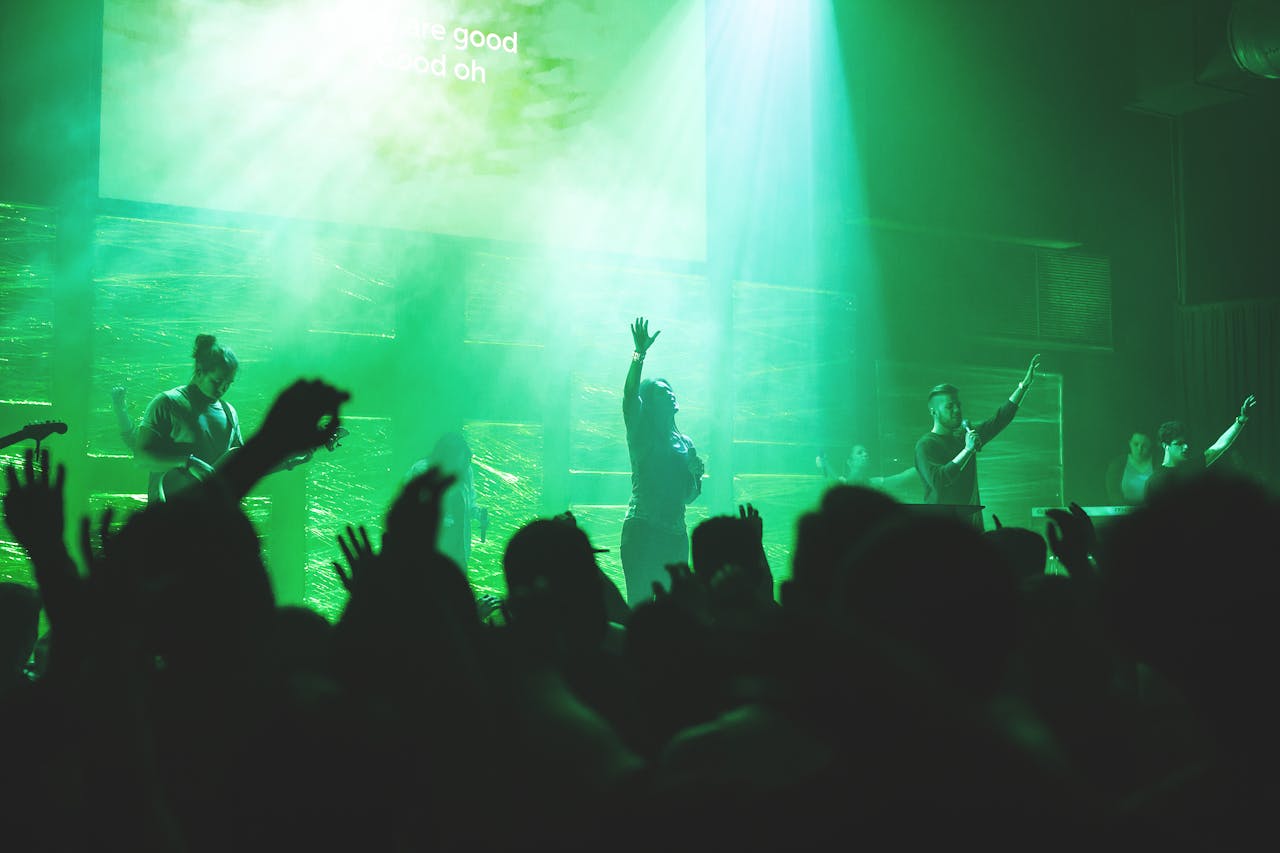 Church worship service in green light with lady on stage raising her hand in praise