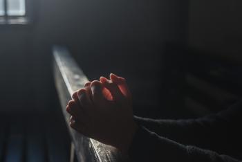 A close-up of clasped hands in prayer resting on a pew.